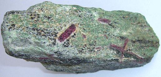This view shows the foliation of the zoisite and hornblende and the cross-cutting nature of the ruby porphyroblasts; also an unusual cross-twin.
